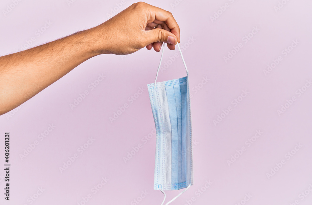 Hand of hispanic man holding medical mask over isolated pink background. Hand of hispanic man holding medical mask over isolated pink background.