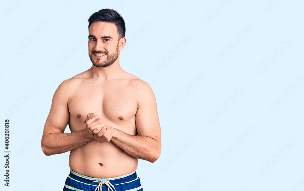 Fototapeta premium Young handsome man wearing swimwear with hands together and crossed fingers smiling relaxed and cheerful. success and optimistic