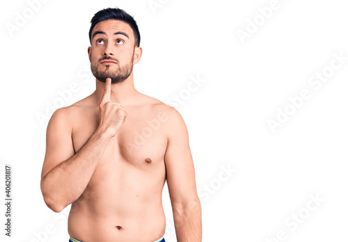 Young handsome man wearing swimwear thinking concentrated about doubt with finger on chin and looking up wondering