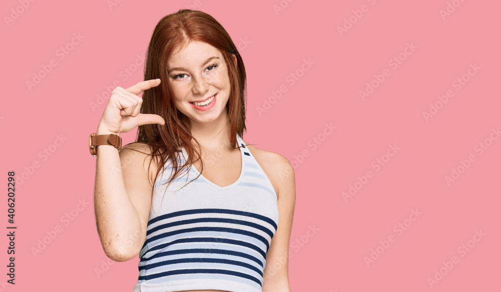 Young read head woman wearing casual clothes smiling and confident gesturing with hand doing small size sign with fingers looking and the camera. measure concept. Young read head woman wearing casual clothes smiling and confident gesturing with hand doing small size sign with fingers looking and the camera. measure concept.