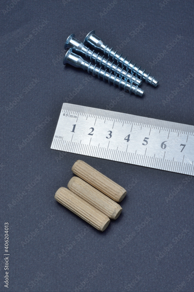 furniture screw, ruler and wooden dowel lie on a dark background. close-up. furniture screw, ruler and wooden dowel lie on a dark background. close-up.