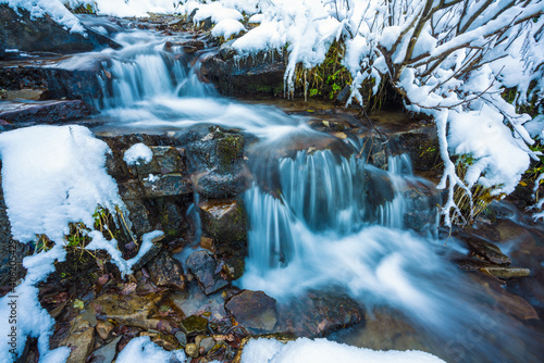 Small stream among wet stones and white snow in the picturesque Carpathian mountains in Ukraine