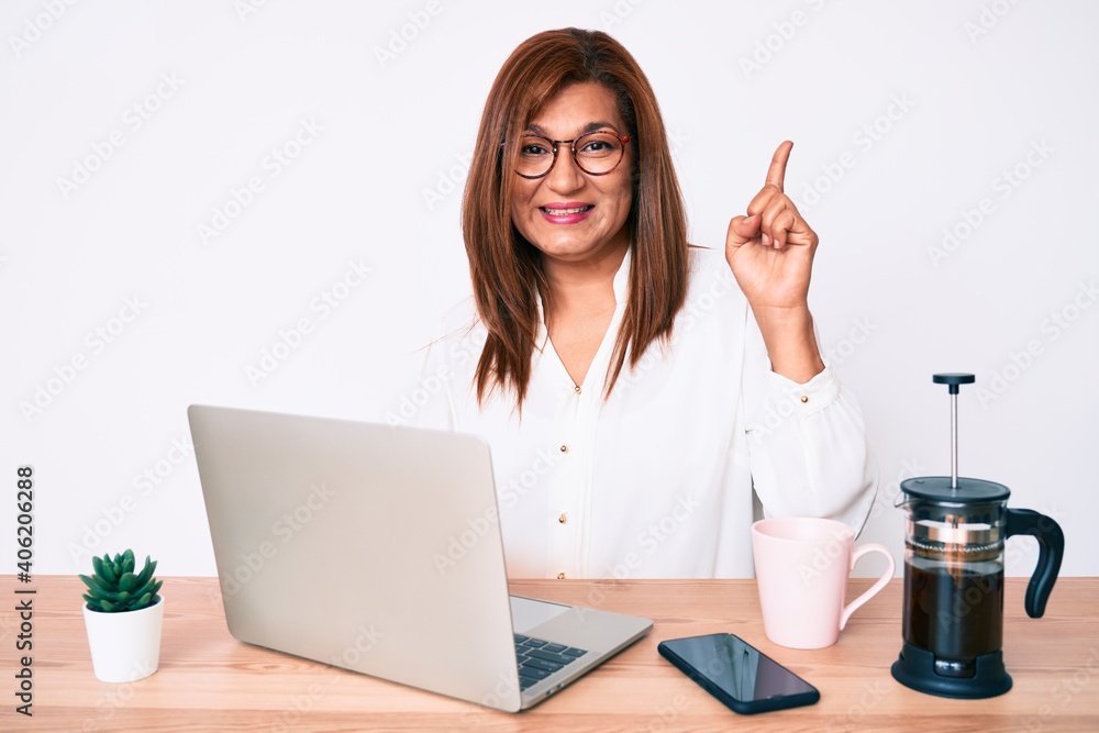 Middle age brunette hispanic business woman working at the office surprised with an idea or question pointing finger with happy face, number one Middle age brunette hispanic business woman working at the office surprised with an idea or question pointing finger with happy face, number one