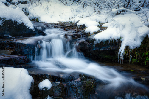 Small stream among wet stones and white snow in the picturesque Carpathian mountains in Ukraine