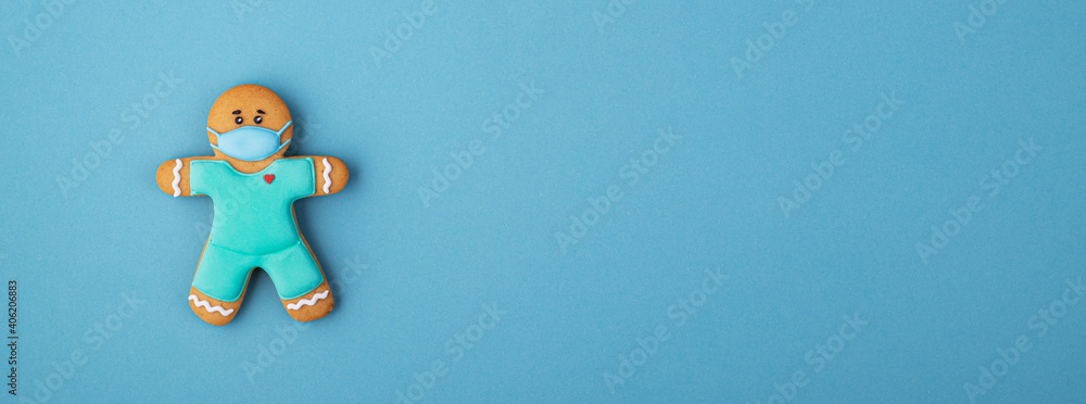 Obraz premium Christmas gingerbread man with a medical mask against a blue background. background for the day of the medic