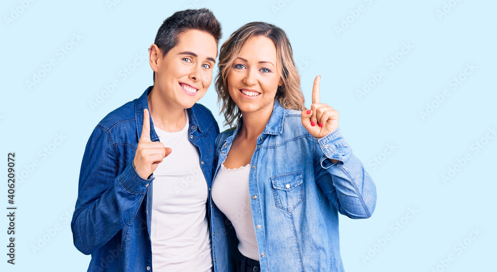 Couple of women wearing casual clothes pointing finger up with successful idea. exited and happy. number one. Couple of women wearing casual clothes pointing finger up with successful idea. exited and happy. number one.