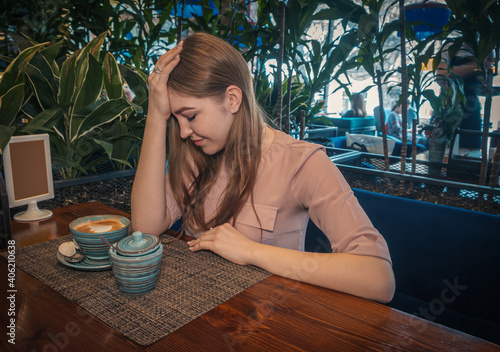 Heartbroken young lady is sitting in cafe and thinking regretfully photo