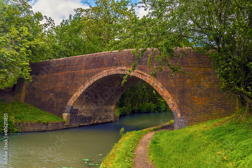 A Victorian brick-built bridge spans the Grand Union Canal near Wistow, UK in summertime