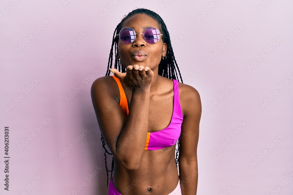 Young african american woman wearing bikini and sunglasses looking at the camera blowing a kiss with hand on air being lovely and sexy. love expression.