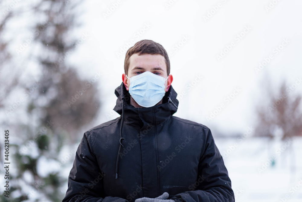 A young guy in winter wears a mask. Young man in protective antiviral mask on the street. The guy in winter clothes in a protective mask. Young man in warm clothes and scarf on a winter day.