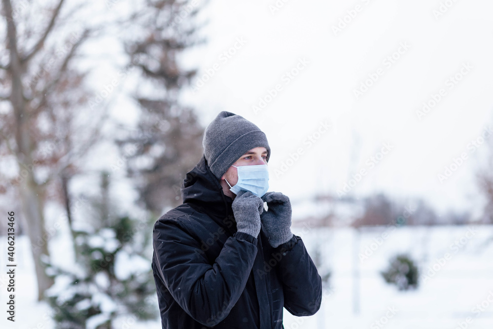 A young guy in winter wears a mask. Young man in protective antiviral mask on the street. The guy in winter clothes in a protective mask. Young man in warm clothes and scarf on a winter day.