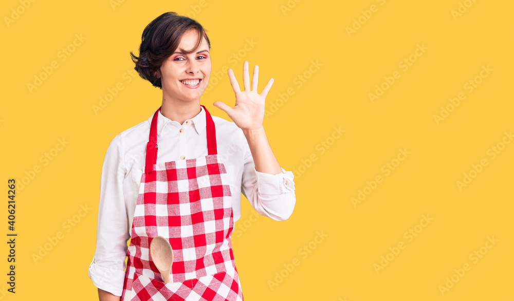 Beautiful young woman with short hair wearing professional cook apron showing and pointing up with fingers number five while smiling confident and happy. Beautiful young woman with short hair wearing professional cook apron showing and pointing up with fingers number five while smiling confident and happy.