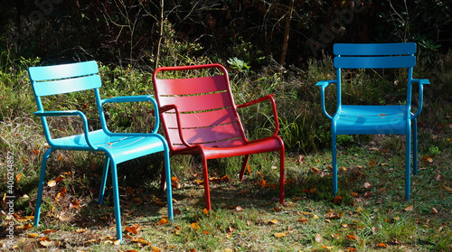 Chairs in the park. Three colorful empty garden seats standing in the grass. Blue, red and green © Wolfborn Indiearts