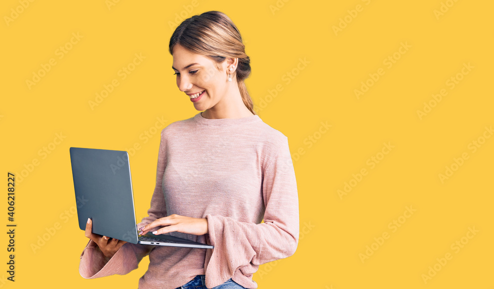 Naklejka premium Beautiful caucasian woman with blonde hair working using computer laptop looking positive and happy standing and smiling with a confident smile showing teeth