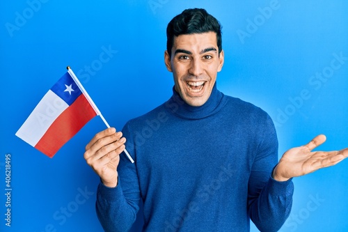 Handsome hispanic business man holding chile flag celebrating achievement with happy smile and winner expression with raised hand