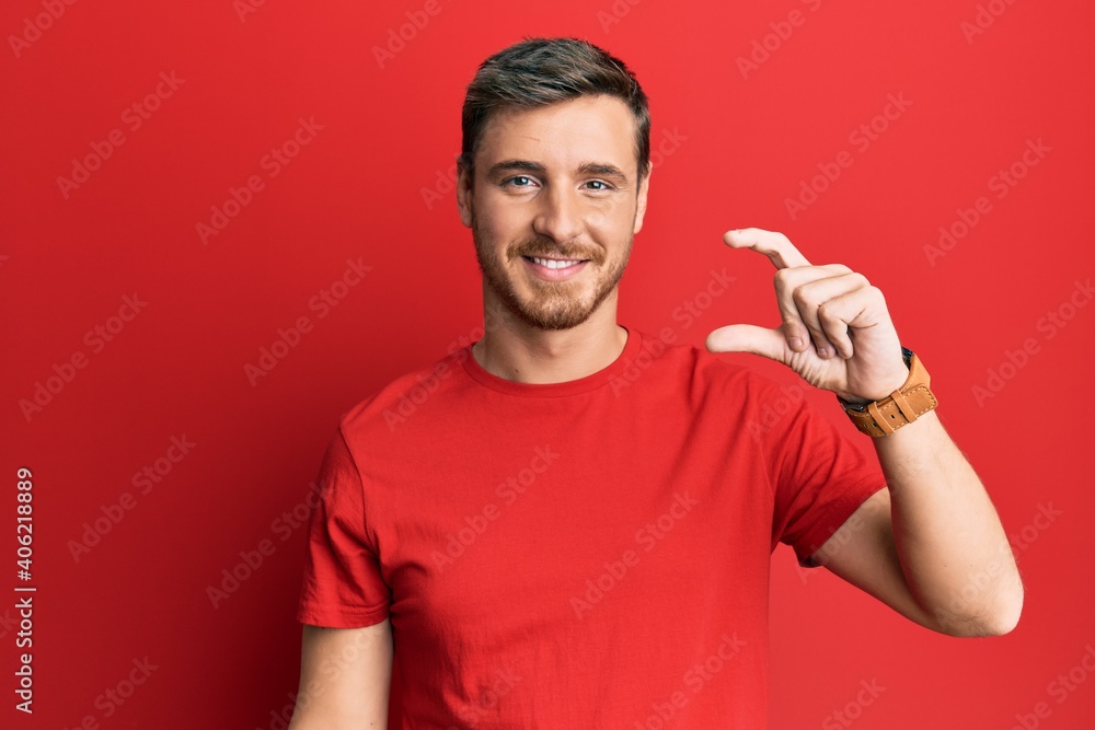 Handsome caucasian man wearing casual red tshirt smiling and confident gesturing with hand doing small size sign with fingers looking and the camera. measure concept. Handsome caucasian man wearing casual red tshirt smiling and confident gesturing with hand doing small size sign with fingers looking and the camera. measure concept.
