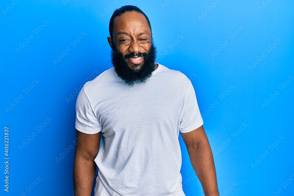 Young african american man wearing casual white tshirt winking looking at the camera with sexy expression, cheerful and happy face. Young african american man wearing casual white tshirt winking looking at the camera with sexy expression, cheerful and happy face.