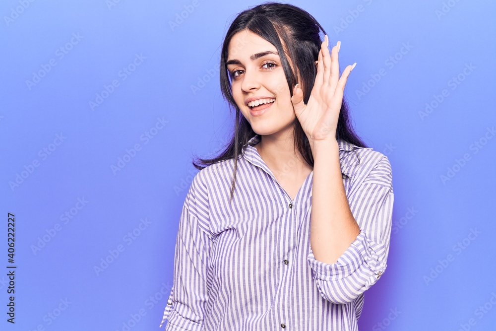 Young beautiful girl wearing casual striped shirt smiling with hand over ear listening and hearing to rumor or gossip. deafness concept. Young beautiful girl wearing casual striped shirt smiling with hand over ear listening and hearing to rumor or gossip. deafness concept.