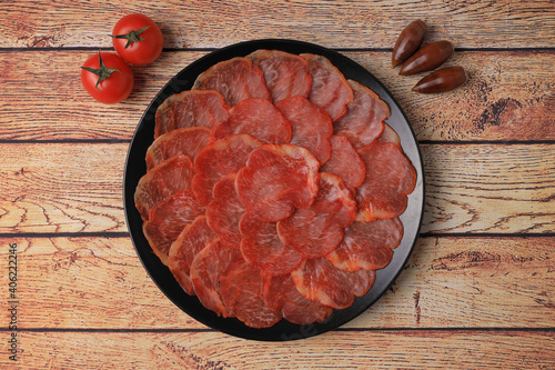 Portion of acorn-fed Iberian loin on a black plate on a wooden table decorated with acorns and tomatoes