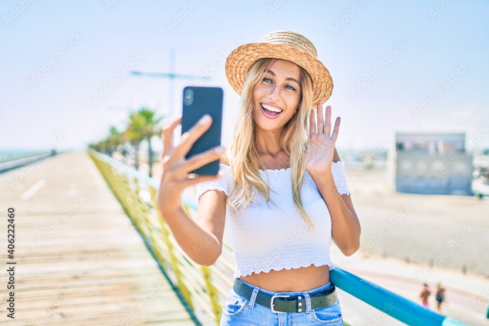 Young blonde tourist girl smiling happy doing video call using smartphone at the promenade.
