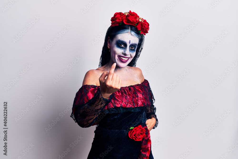Young woman wearing mexican day of the dead makeup beckoning come here gesture with hand inviting welcoming happy and smiling Young woman wearing mexican day of the dead makeup beckoning come here gesture with hand inviting welcoming happy and smiling