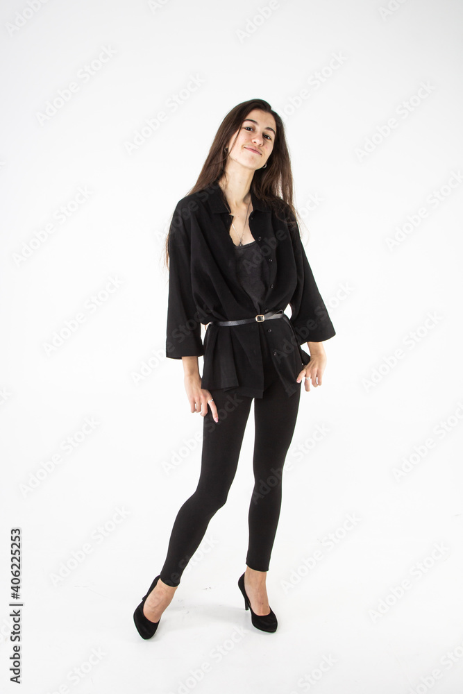 Beautiful young woman with long brown hair in black black blazer and leggings posing on white background Beautiful young woman with long brown hair in black black blazer and leggings posing on white background