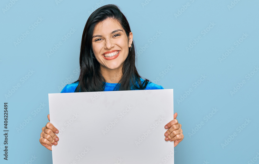 Young hispanic woman holding blank empty banner looking positive and happy standing and smiling with a confident smile showing teeth Young hispanic woman holding blank empty banner looking positive and happy standing and smiling with a confident smile showing teeth