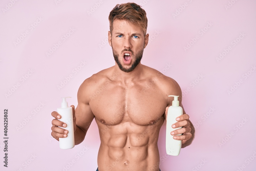 Young caucasian man shirtless holding cream lotion afraid and shocked with surprise and amazed expression, fear and excited face. Young caucasian man shirtless holding cream lotion afraid and shocked with surprise and amazed expression, fear and excited face.
