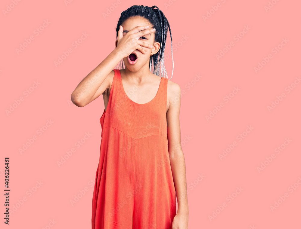 Fototapeta premium Cute african american girl wearing casual clothes peeking in shock covering face and eyes with hand, looking through fingers with embarrassed expression.