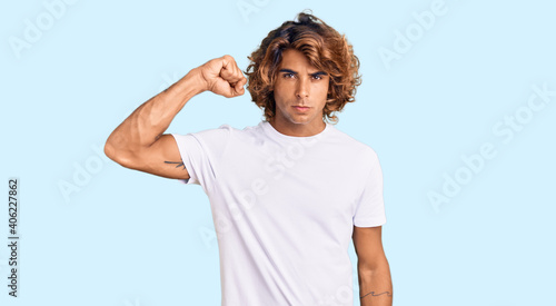 Young hispanic man wearing casual white tshirt strong person showing arm muscle, confident and proud of power
