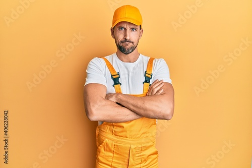Young handsome man wearing handyman uniform over yellow background skeptic and nervous  disapproving expression on face with crossed arms. negative person.