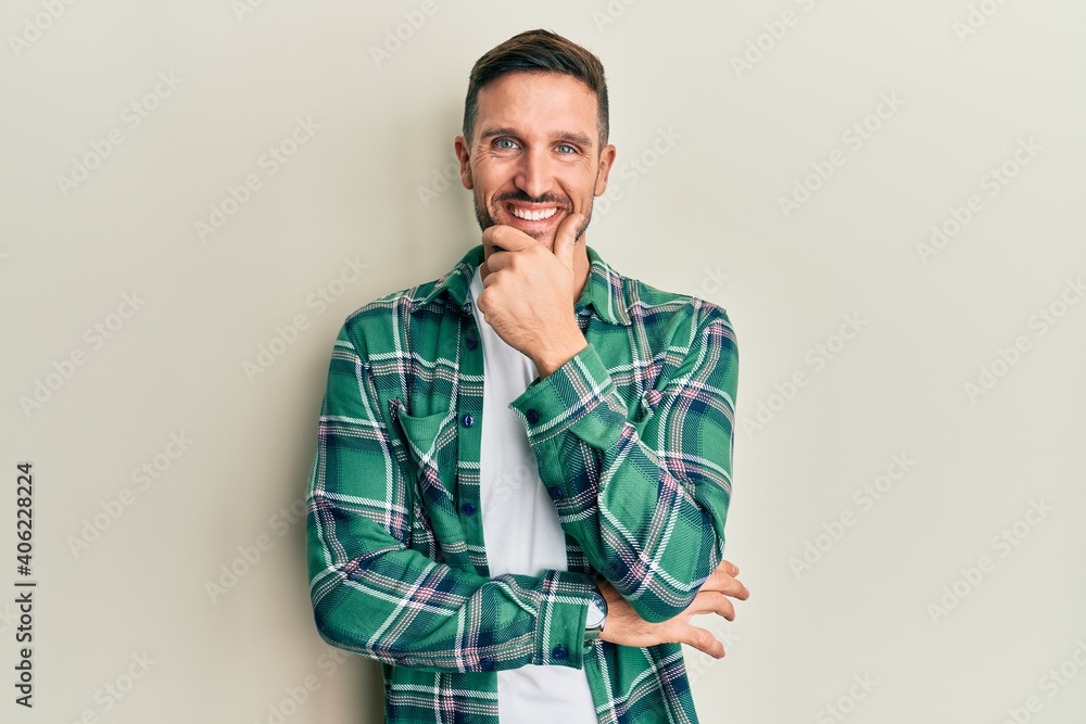 Handsome man with beard wearing casual clothes looking confident at the camera smiling with crossed arms and hand raised on chin. thinking positive. Handsome man with beard wearing casual clothes looking confident at the camera smiling with crossed arms and hand raised on chin. thinking positive.