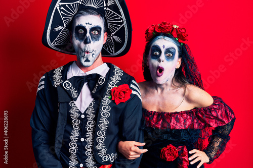 Young couple wearing mexican day of the dead costume over red afraid and shocked with surprise expression, fear and excited face.