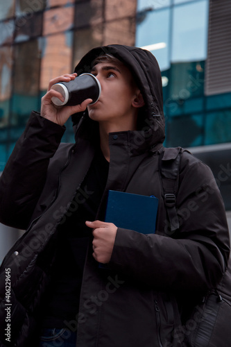 A young man walking down the street and drinking coffee. Everyday life in a big city. Coffee and books. Street in the winter.
