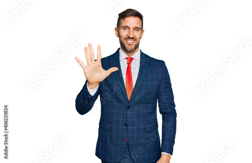 Handsome man with beard wearing business suit and tie showing and pointing up with fingers number five while smiling confident and happy.