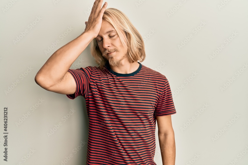 Caucasian young man with long hair wearing casual striped t shirt surprised with hand on head for mistake, remember error. forgot, bad memory concept. Caucasian young man with long hair wearing casual striped t shirt surprised with hand on head for mistake, remember error. forgot, bad memory concept.