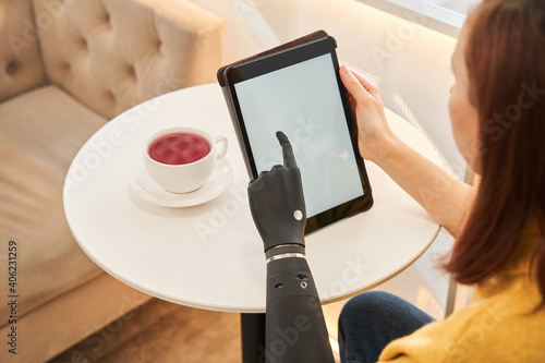 Woman with prosthesis arm using digital tablet at table in cafe
