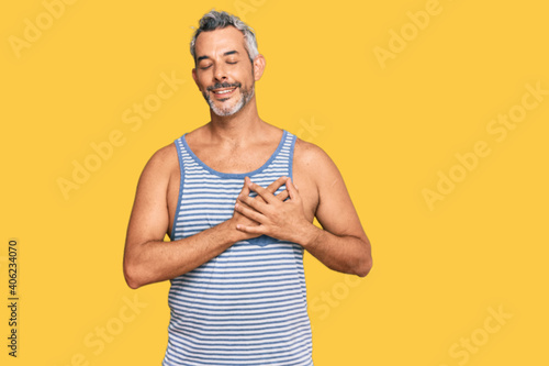Middle age grey-haired man wearing casual style with sleeveless shirt smiling with hands on chest with closed eyes and grateful gesture on face. health concept.