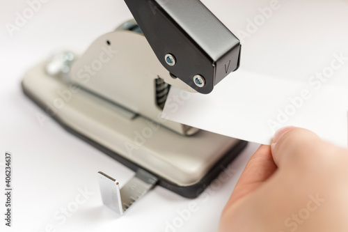 Manual hole punch for installing metal sleeves or eyelets. white tag in hand. close-up