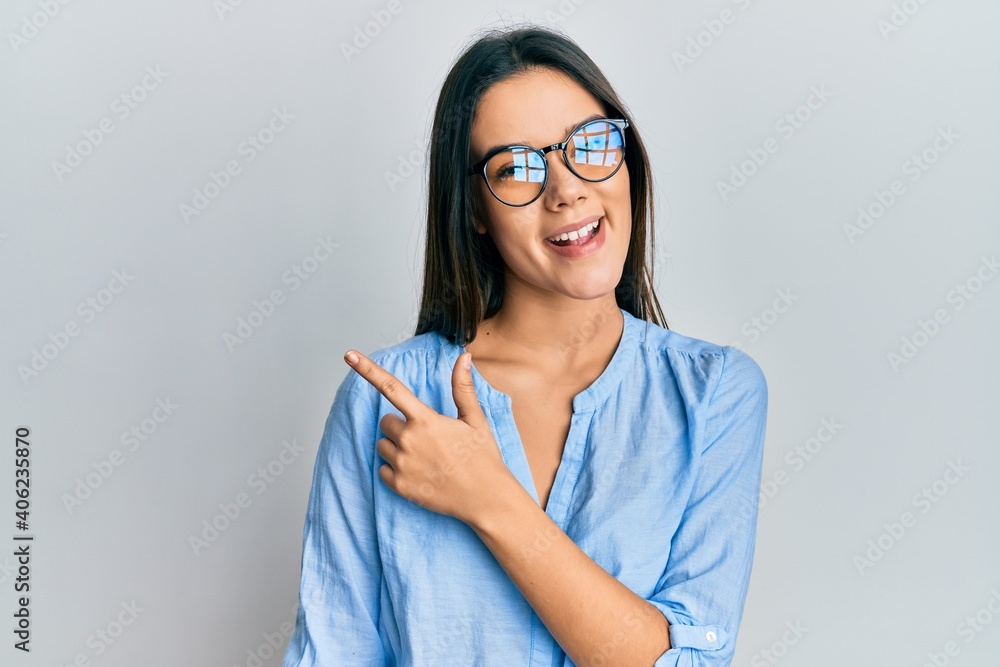 Young hispanic girl wearing casual clothes and glasses smiling cheerful pointing with hand and finger up to the side