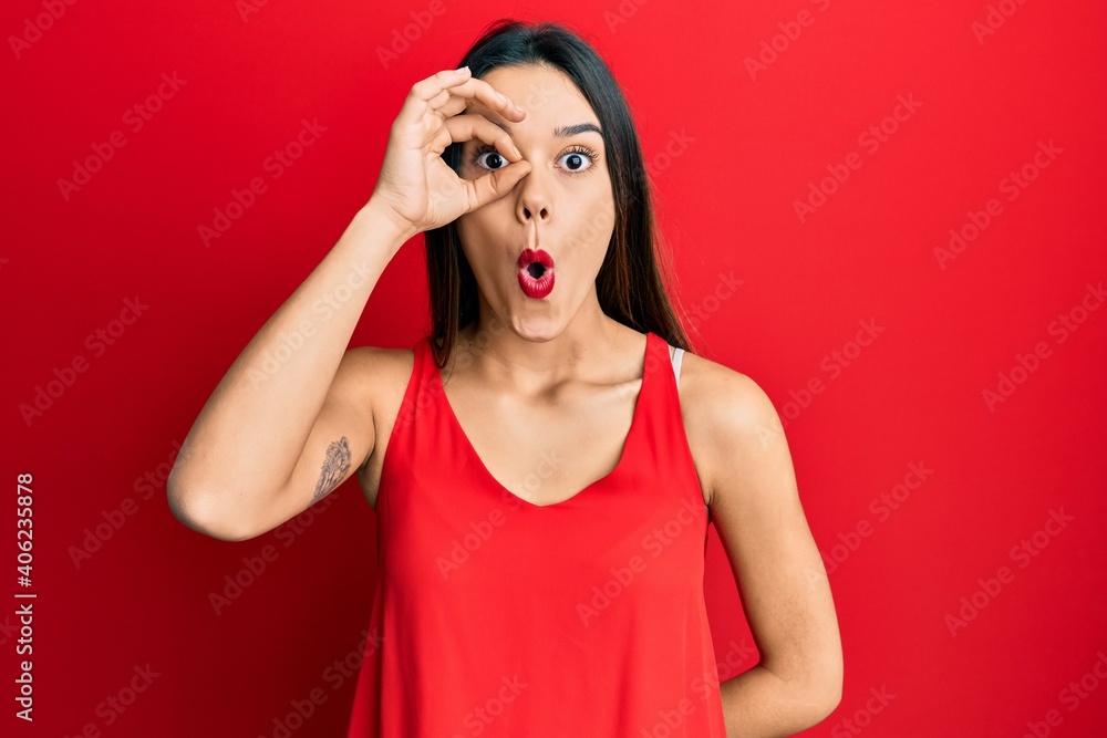 Young hispanic girl wearing casual style with sleeveless shirt doing ok gesture shocked with surprised face, eye looking through fingers. unbelieving expression. Young hispanic girl wearing casual style with sleeveless shirt doing ok gesture shocked with surprised face, eye looking through fingers. unbelieving expression.
