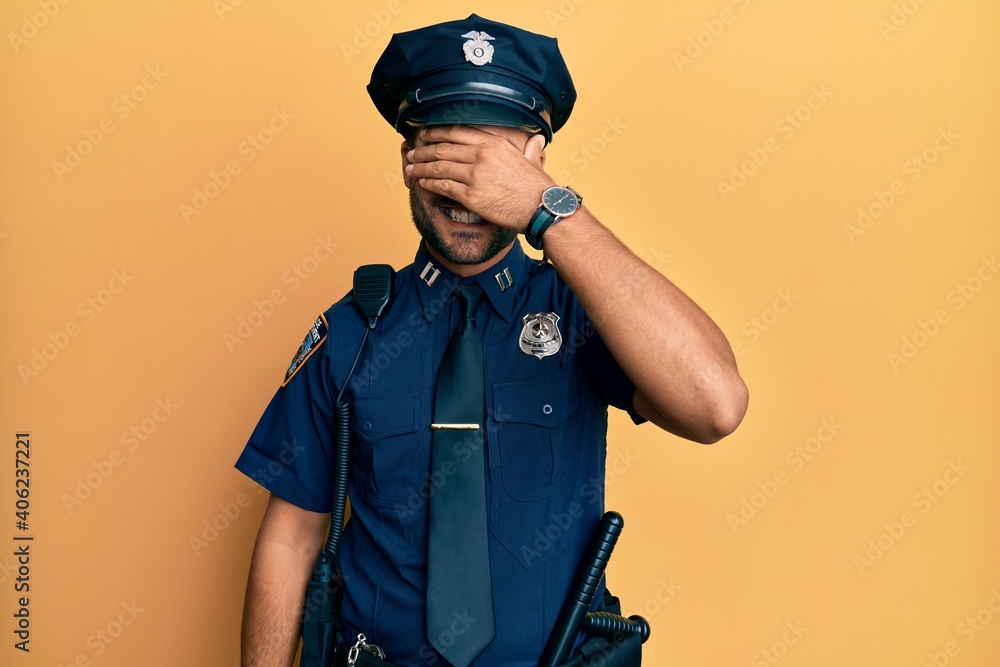 Handsome hispanic man wearing police uniform smiling and laughing with hand on face covering eyes for surprise. blind concept. Handsome hispanic man wearing police uniform smiling and laughing with hand on face covering eyes for surprise. blind concept.