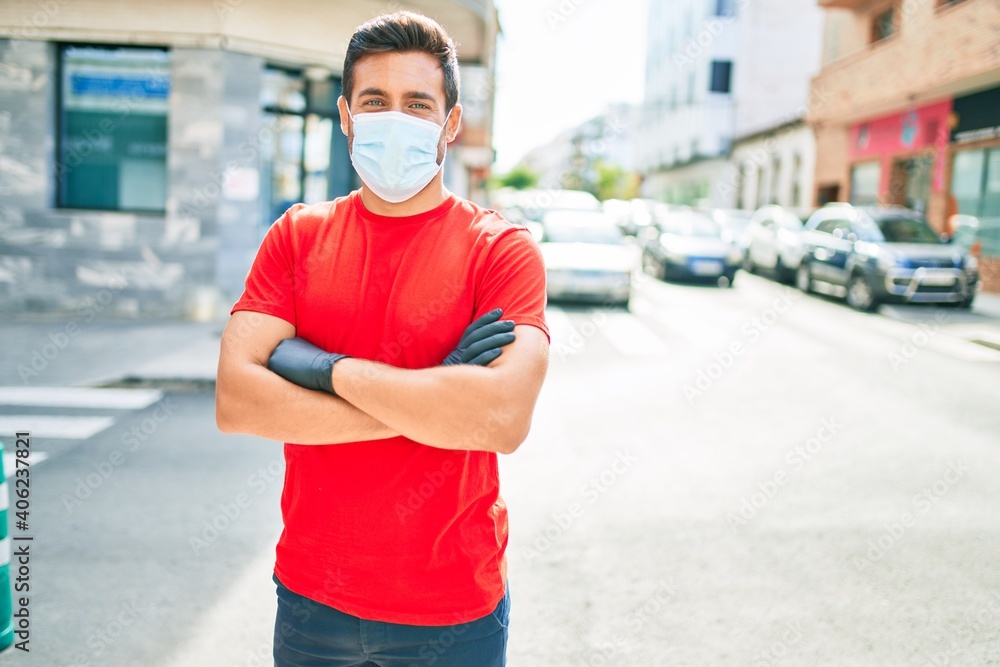 Young handsome hispanic man wearing covid-19 protection medical mask standing at town street.