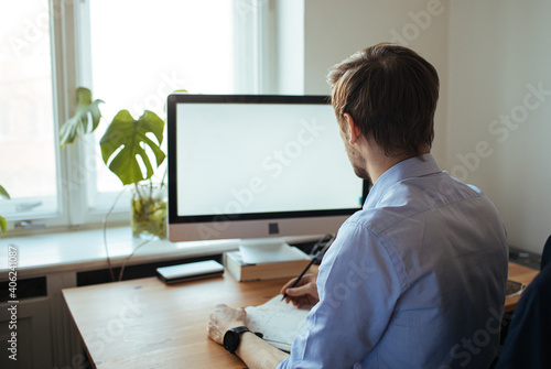 Man working from a home office. Computer with blank empty screen for copy space and information. A businessman from behind shoulder view. A creative entrepreneur