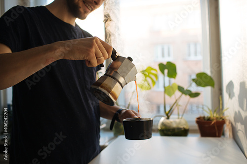 Man making morning coffee in moka espresso pot. Flavorful coffee at home kitchen. Male pouring coffee in a cup. Guy morning cozy ritual. Breakfast lighter roast blend. Home leisure fika at holidays	

