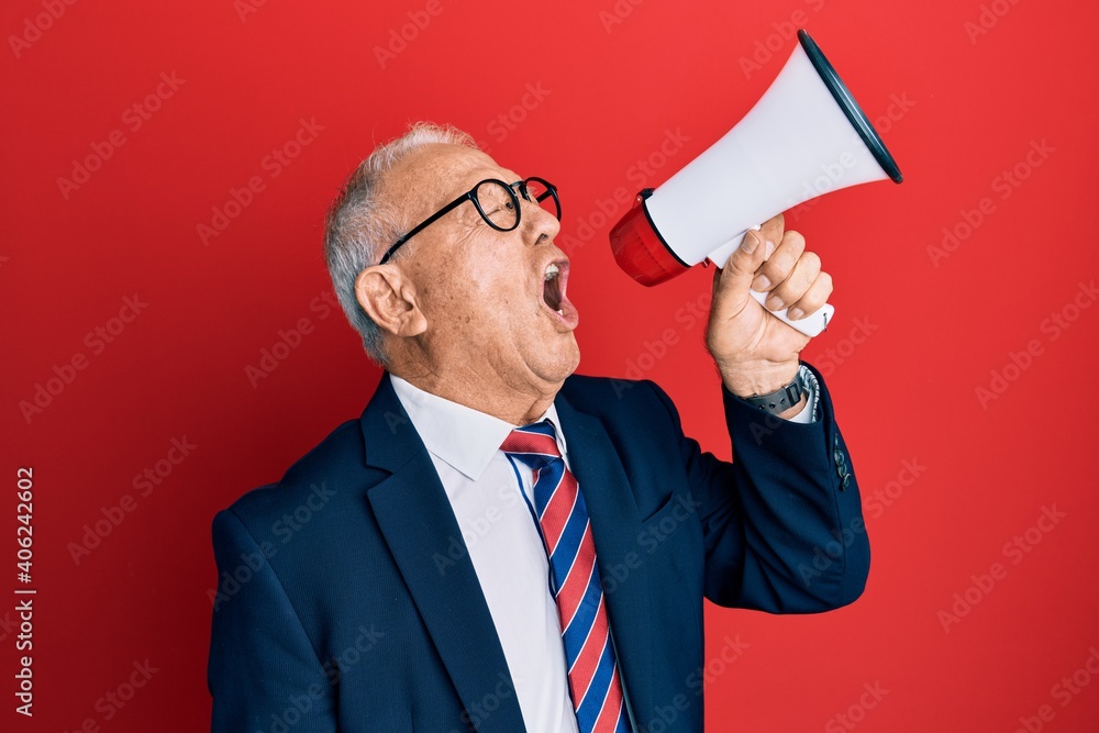 Senior grey-haired businessman screaming using megaphone over isolated red background. Senior grey-haired businessman screaming using megaphone over isolated red background.