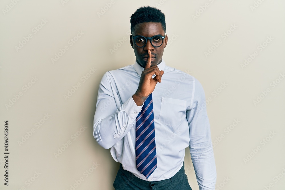 Fototapeta premium Handsome black man wearing glasses business shirt and tie asking to be quiet with finger on lips. silence and secret concept.