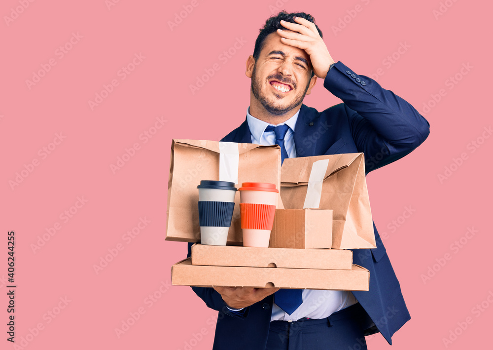 Young hispanic man wearing suit holding takeaway coffee and food stressed and frustrated with hand on head, surprised and angry face Young hispanic man wearing suit holding takeaway coffee and food stressed and frustrated with hand on head, surprised and angry face
