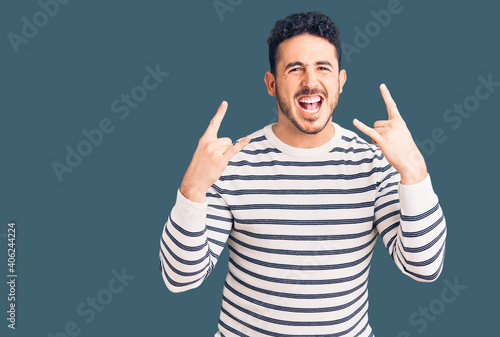 Young hispanic man wearing casual clothes shouting with crazy expression doing rock symbol with hands up. music star. heavy music concept.