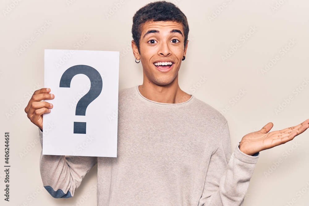 Young african amercian man holding question mark celebrating achievement with happy smile and winner expression with raised hand